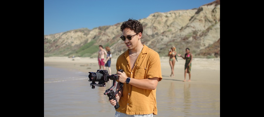 DiLA Student capturing video on the beach in sunglasses SU2023 CR:TessaMartinko